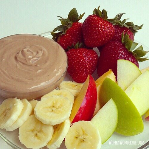 creamy nutella dip next to sliced bananas, apples and whole strawberries