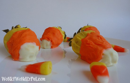 four strawberries covered in yellow, orange and white candy coating to resemble a candy corn