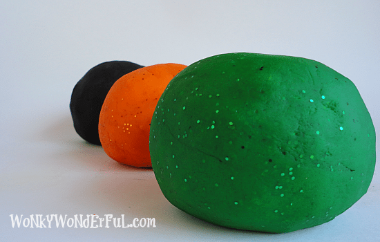 green, orange and black play dough balls in a row