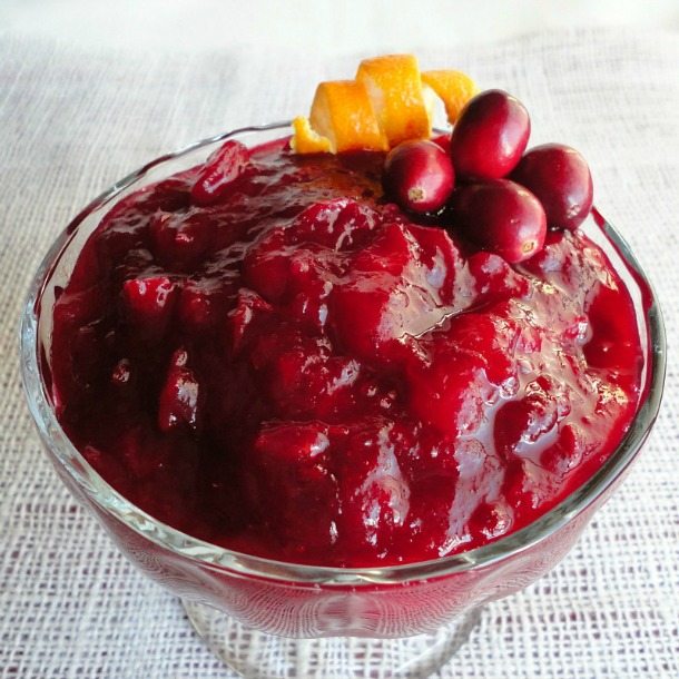 deep red cranberry sauce topped with fresh cranberries and orange zest in clear glass dish