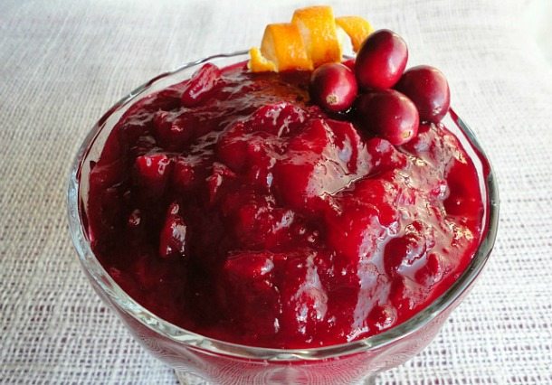 deep red cranberry sauce topped with fresh cranberries and orange zest in clear glass dish