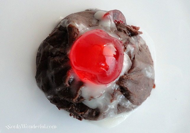close up of brown cookie topped with bright red candy cherry