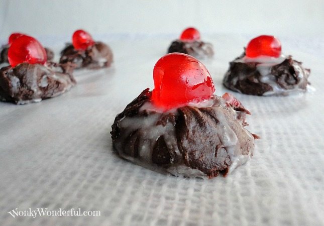 chocolate cookies dripping with white glaze and topped with a bright red candied cherry