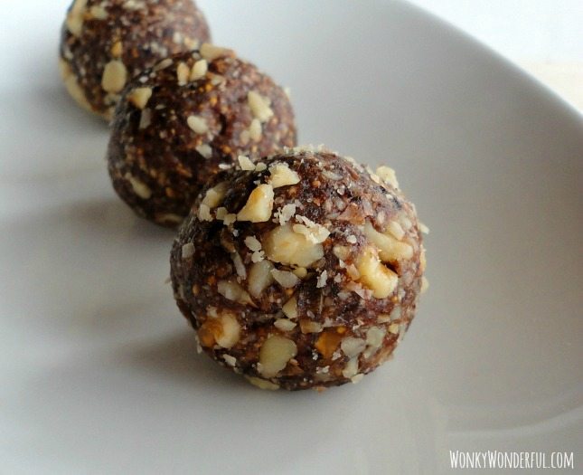 ball shaped energy bites that are dark brown with pieces of walnuts in them, on white plate