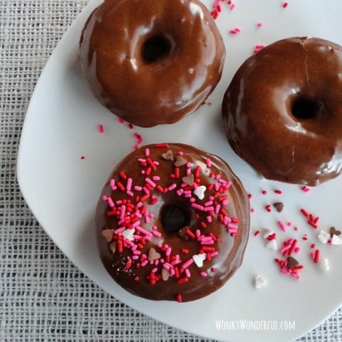 three chocolate donuts topped with nutella glaze and sprinkles on white plate