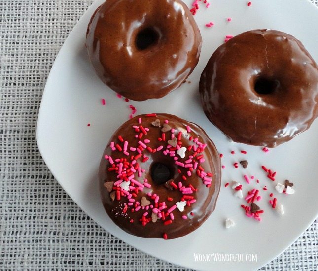 three chocolate donuts topped with nutella glaze and sprinkles on white plate