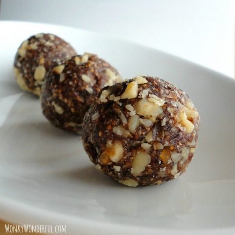 ball shaped energy bites that are dark brown with pieces of walnuts in them, on white plate