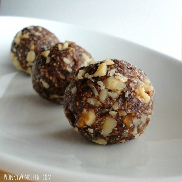 ball shaped energy bites that are dark brown with pieces of walnuts in them, on white plate