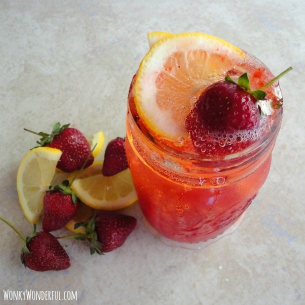 fizzy drink with lemon and strawberry on top in clear glass mason jar, lemons and strawberries on the side