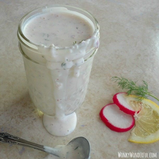 ranch dressing dripping over the side of clear glass jar next to sliced radishes, lemon slice and a spoon