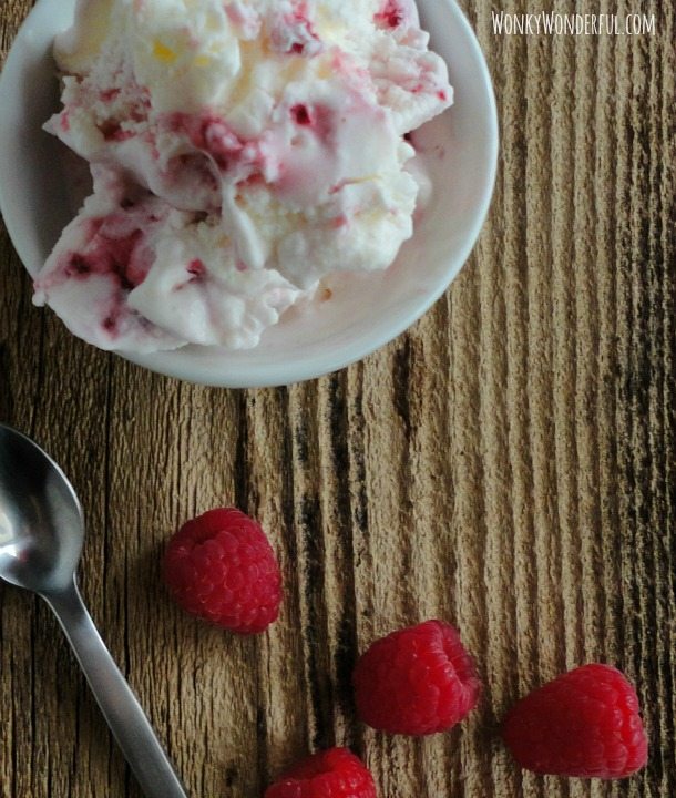white bowl filled with ice cream with spoon and fresh raspberries on the side