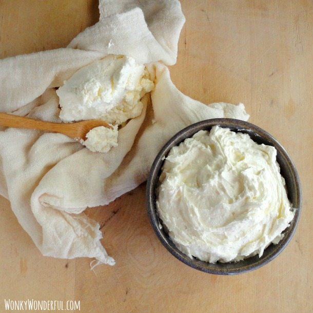 Homemade Ricotta in dark bowl next to cheesecloth and spoon with riocotta on it