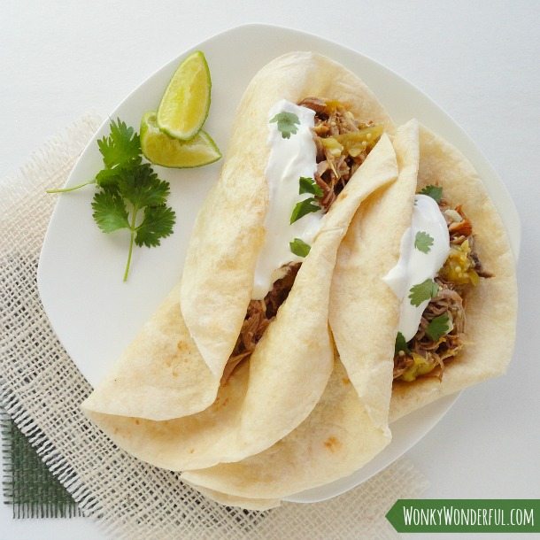 two tacos on white plate with cilantro and lime wedges on the side