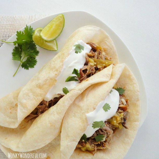 two tacos on white plate with cilantro and lime wedges on the side
