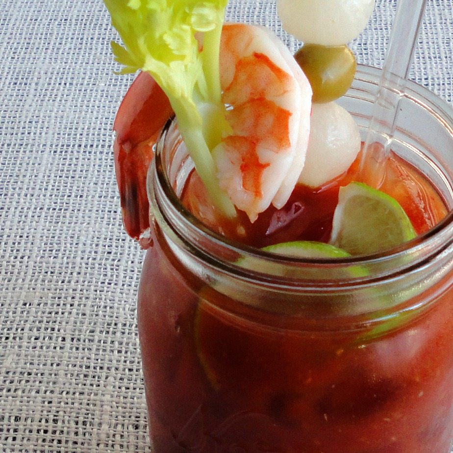 top view of red cocktail in glass jar topped with shrimp, celery and limes