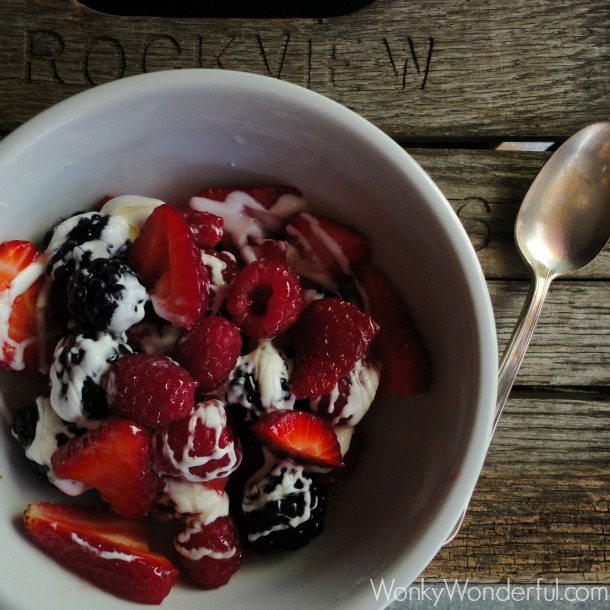 white bowl filled with berries drizzled with creme fraiche