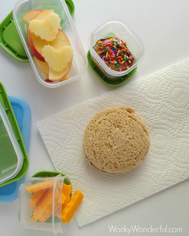 top view of round sandwich, cut apples, crinkle cheddar cheese and peanut butter topped with sprinkles