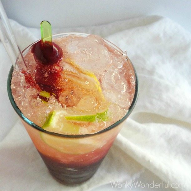 clear tall glass with dark red liquid, ice and lime slices