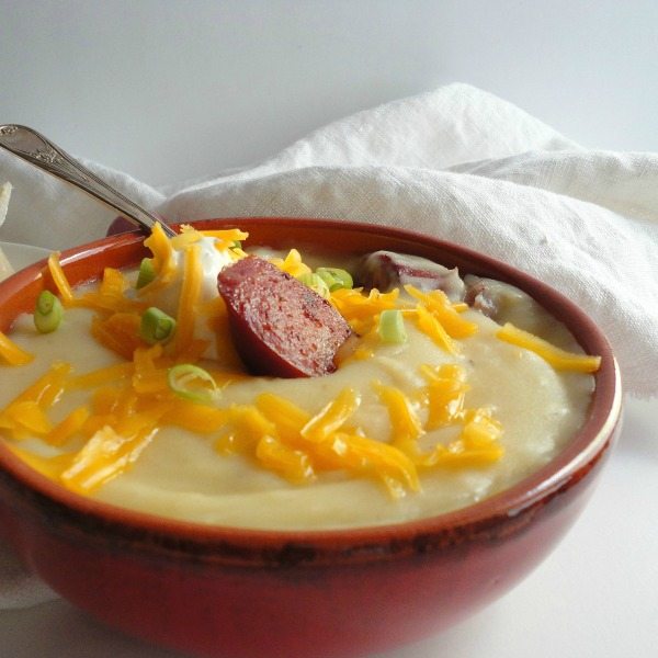 red bowl filled with creamy potato soup topped with sausage and shredded cheese