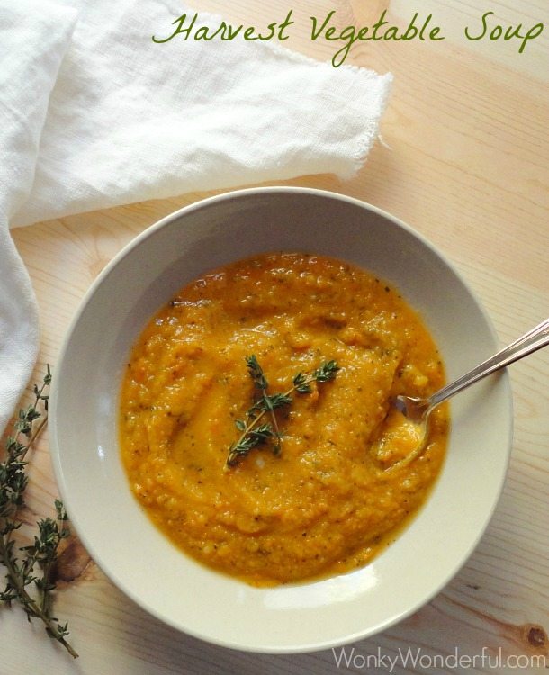 orange pureed soup topped with fresh thyme in beige bowl