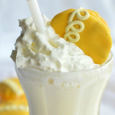 clear glass milkshake cup filled with creamy white shake and topped with whipped cream and an orange cupcake