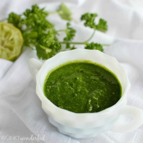 white dish filled with dark green sauce with fresh herbs on the side