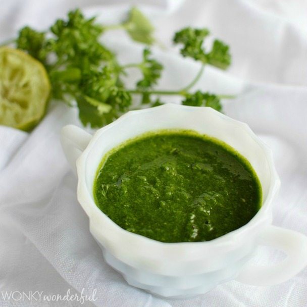 white dish filled with dark green sauce with fresh herbs on the side