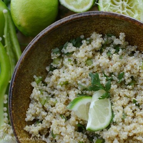 cooked quinoa topped with sliced limes and chopped cilantro in brown bowl