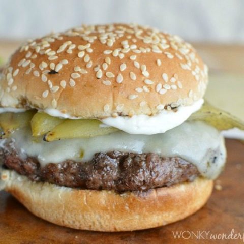 grilled burger with cheese and a green Chile on a sesame seed bun