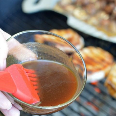 hand holding bbq brush and clear glass bowl filled with bbq sauce
