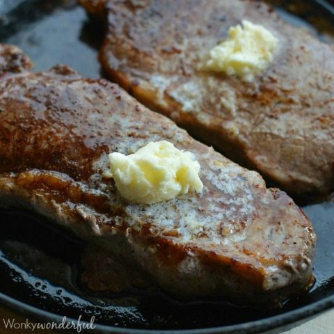 two cooked steaks topped with butter in cast iron pan
