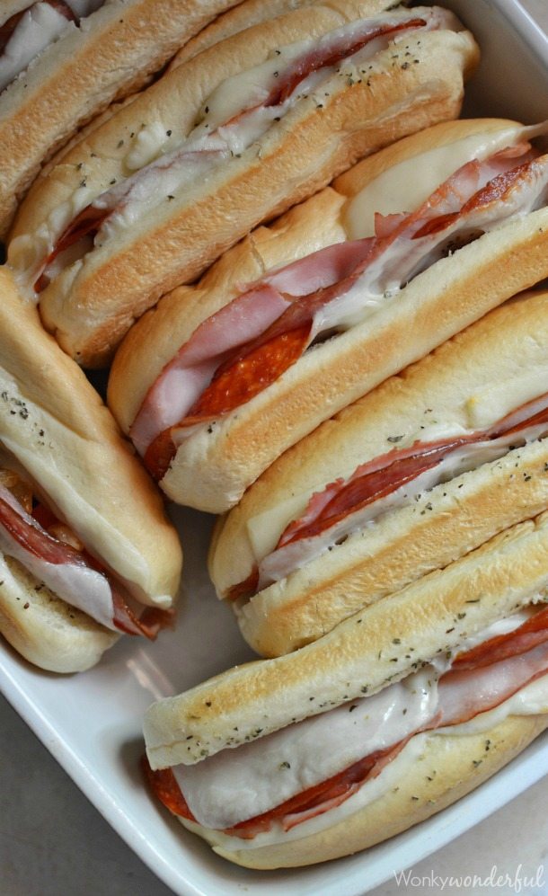 Hot Italian Sandwiches baked in the oven. Meaty Cheesy Sub Sandwiches, great for feeding a large crowd! #easydinner #gamedayfood #sandwiches italian sandwiches in roasting dish with melty cheese