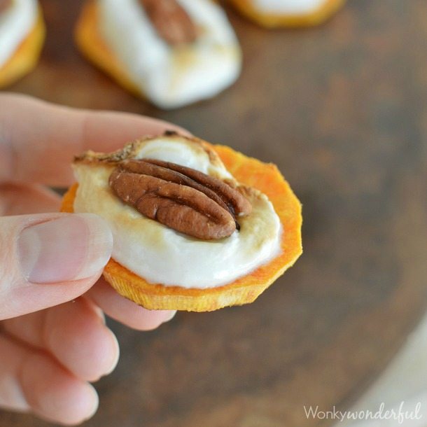 hand holding sliced sweet potato topped with a marshmallow and pecan