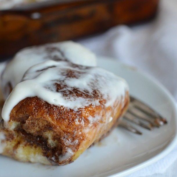 brown cinnamon roll topped with white glaze served on white plate with fork