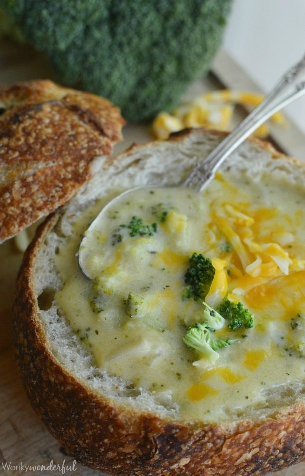 hollow bread bowl filled with soup and topped with broccoli and shredded cheese