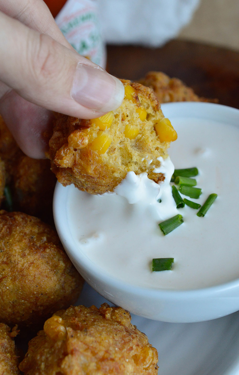 hand dipping fritter into sauce