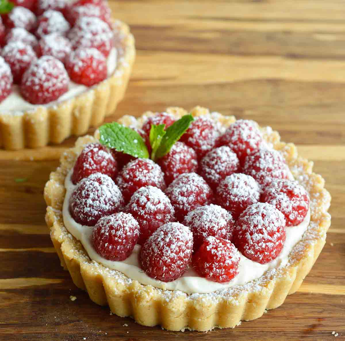 This Gluten Free Raspberry Tart Recipe will complete any holiday meal! A buttery gf tart crust filled with whipped vanilla cheesecake and topped with fresh raspberries. An easy, festive and delicious holiday dessert!