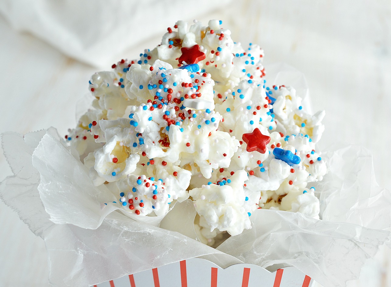 Make an easy and festive treat to enjoy while watching the fireworks. 4th of July Dessert Popcorn is popped microwave popcorn drizzled with white chocolate and topped with Red, White and Blue sprinkles! This patriotic dessert recipe is perfect for feeding a crowd!