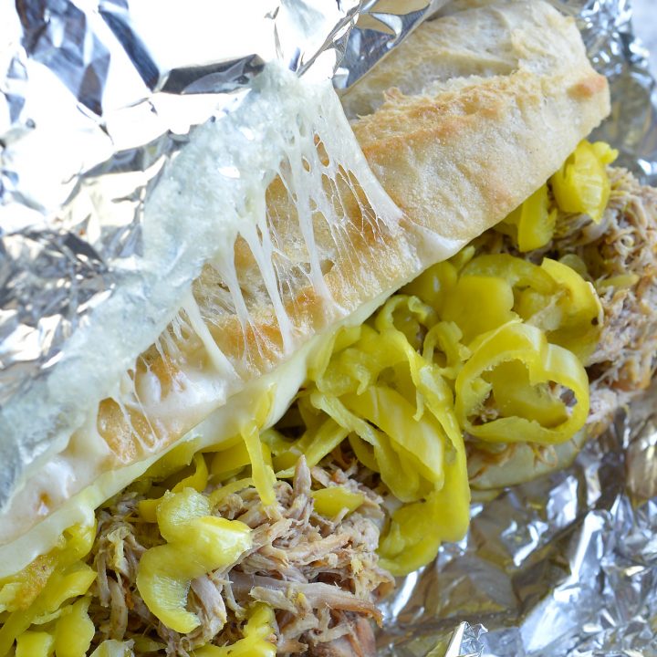 If you are tired of the same old barbecue pork sandwiches give these Slow Cooker Pulled Pork Cuban Sandwiches a try! This easy dinner recipe is inspired by Cuban Sandwiches. Start with Coca-Cola slow cooker pulled pork then add cheese, pepperoncinis, pickles, mustard and bread. These oven baked sandwiches are perfect for feeding a crowd!