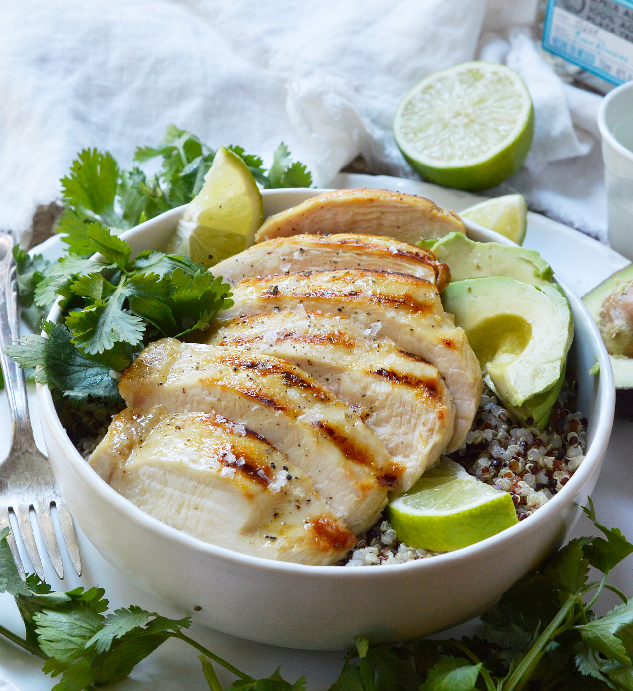 sliced tequila lime chicken breast over quinoa with limes, cilantro and avocado on the side