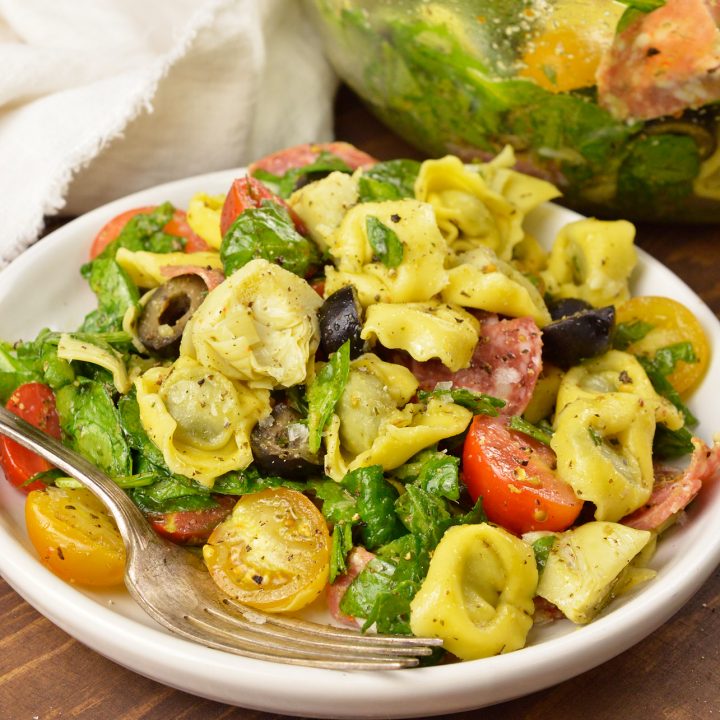 tortellini pasta salad with spinach, olives and tomatoes on white plate with fork