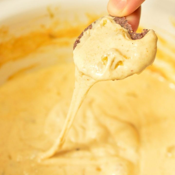 hand dipping chip into melty cheese quest dip