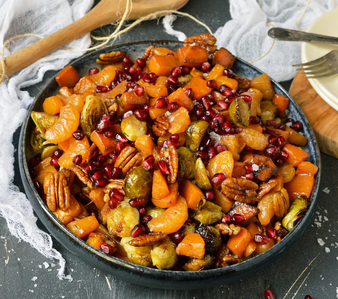 blue serving bowl filled with butternut squash chunks, orange segments, pecans and pomegranate seeds