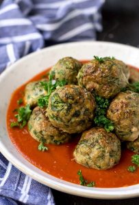 baked turkey meatballs with spinach in white bowl with red sauce