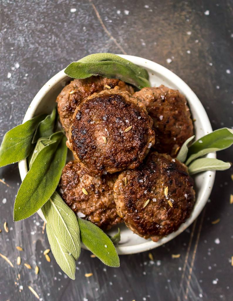 overhead photo of breakfast sausages surrounded be fresh green sage