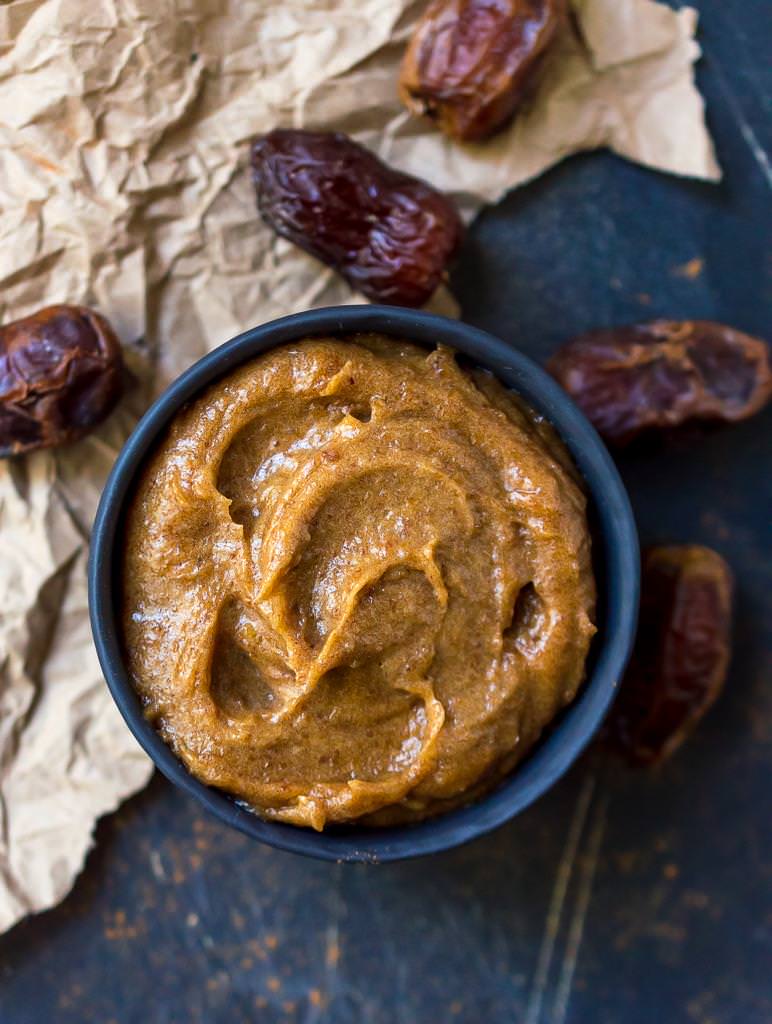 over head photo of creamy date paste in black bowl. Dates and crumpled brown paper in the background.