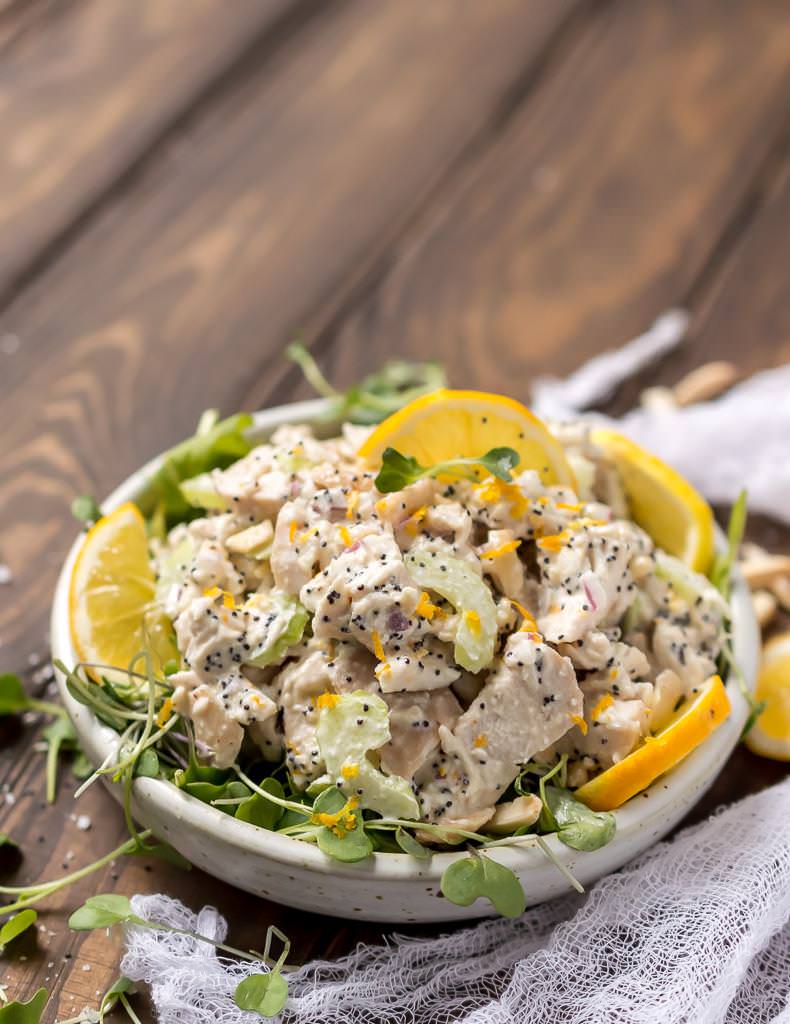 full view of white bowl filled with poppy seed lemon chicken salad. white cheesecloth on the side