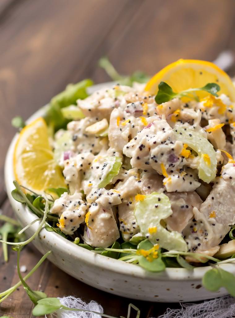 side view close up of lemon chicken salad with black poppy seeds and bright yellow lemon slices