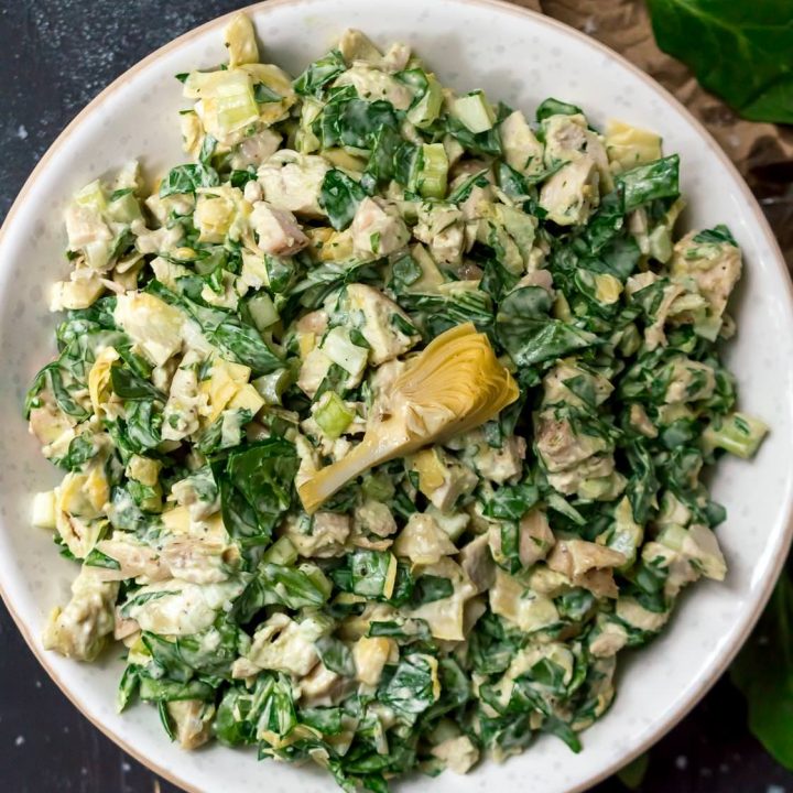 close up over head photo of green spinach artichoke chicken salad in white bowl