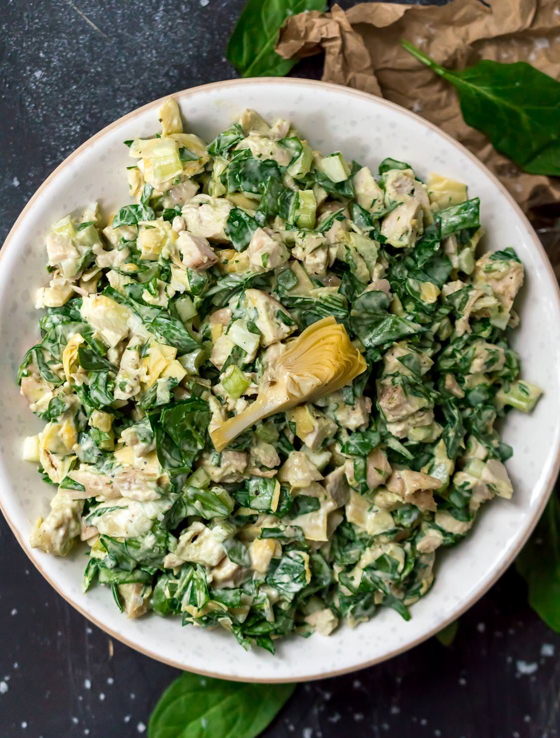 close up over head photo of green spinach artichoke chicken salad in white bowl